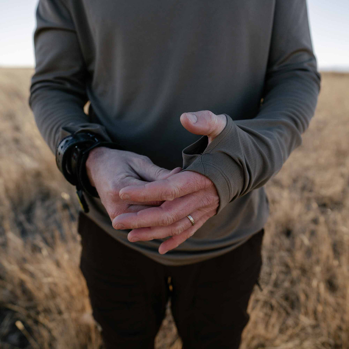 Person wearing a dark olive green long-sleeve shirt with thumbholes on the cuffs.
