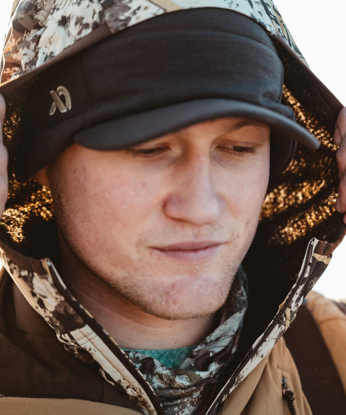 Black baseball cap with curved brim and 'cx' logo, worn under a camo hood.