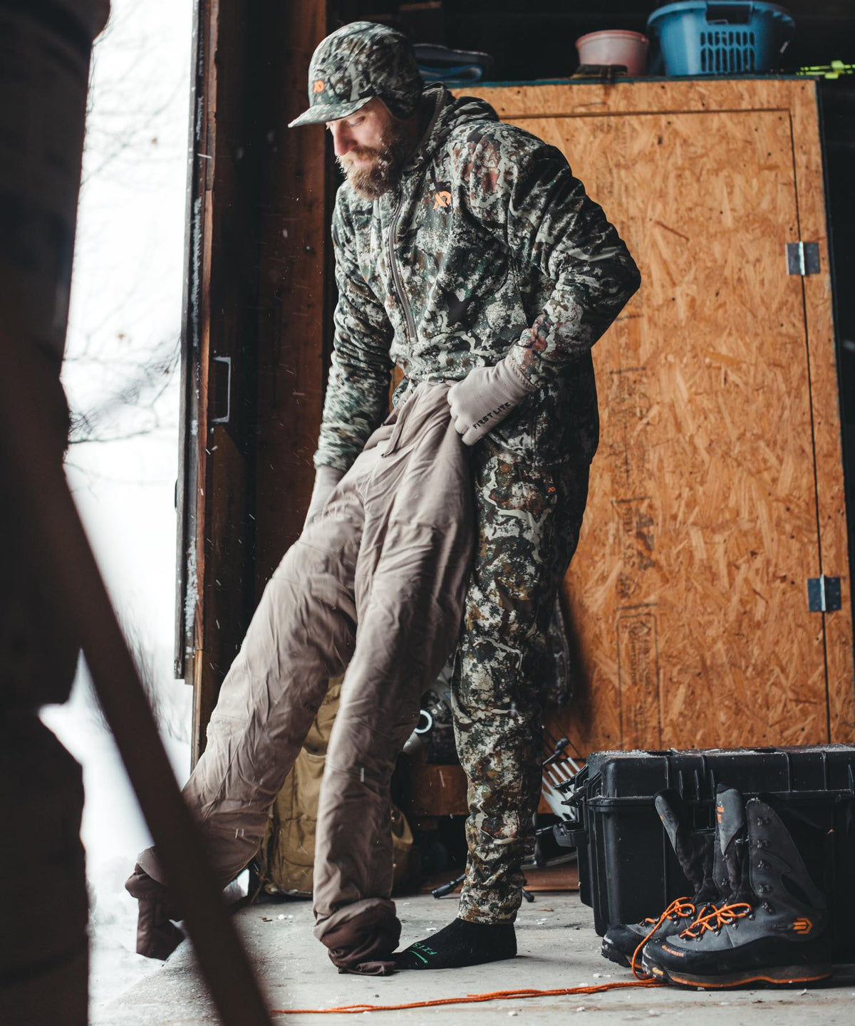 Man in First Lite camo pulling on tan insulated hunting pants.