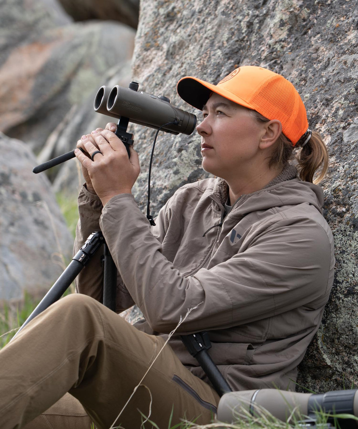 Olive green SigSauer binoculars on tripod, held by woman in orange hat.