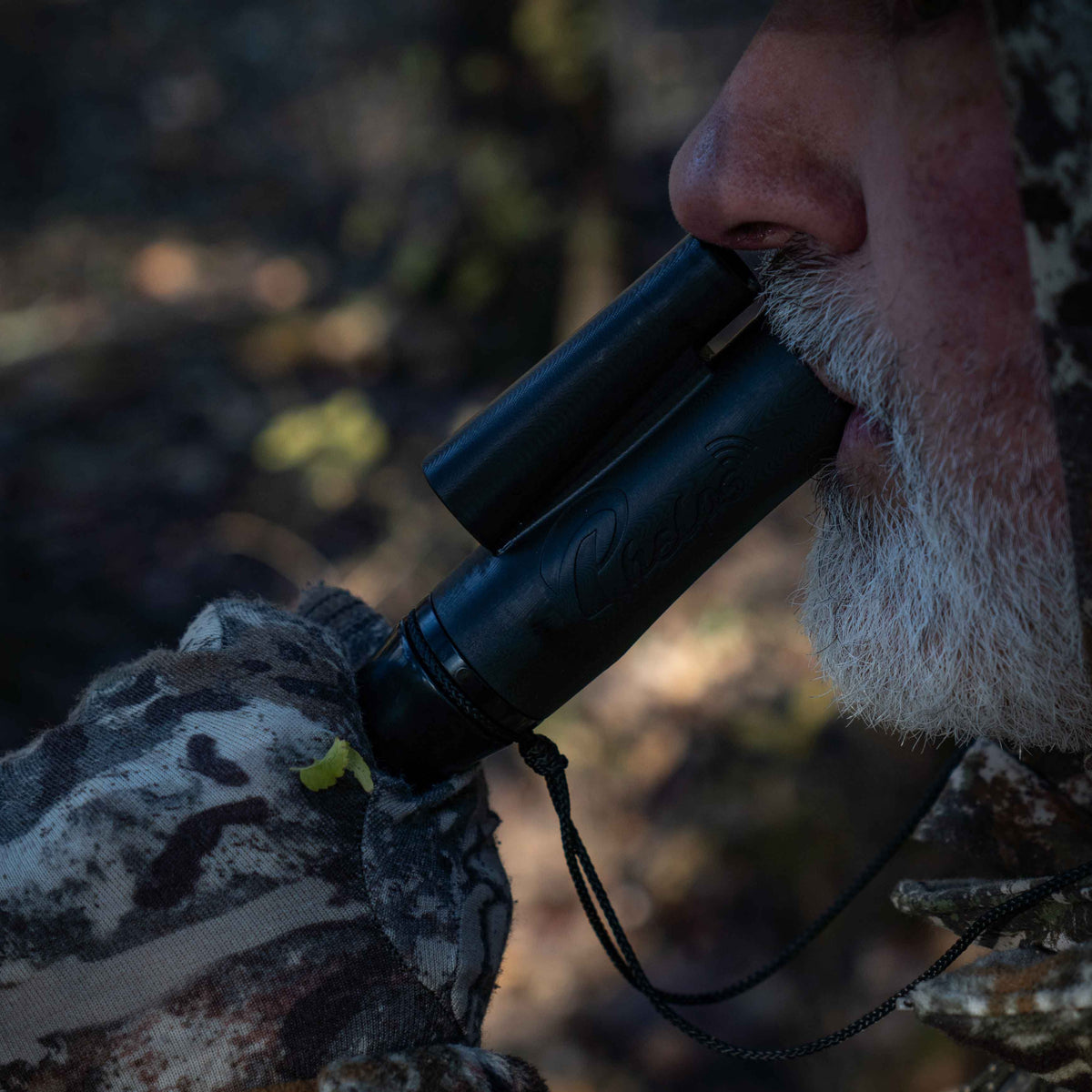 A bearded hunter uses a black Primos two-part game call, held to his mouth and nose.