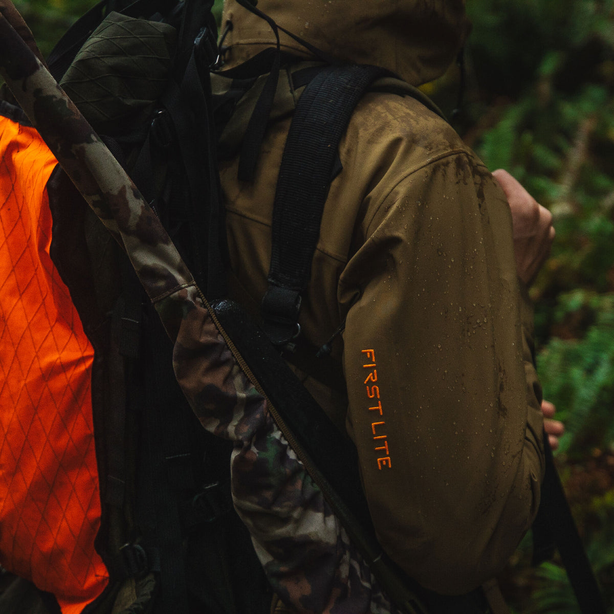 Olive-brown 'FIRST LITE' jacket, wet with raindrops, worn by a person carrying a backpack with a camouflage rifle case and orange visibility panel.