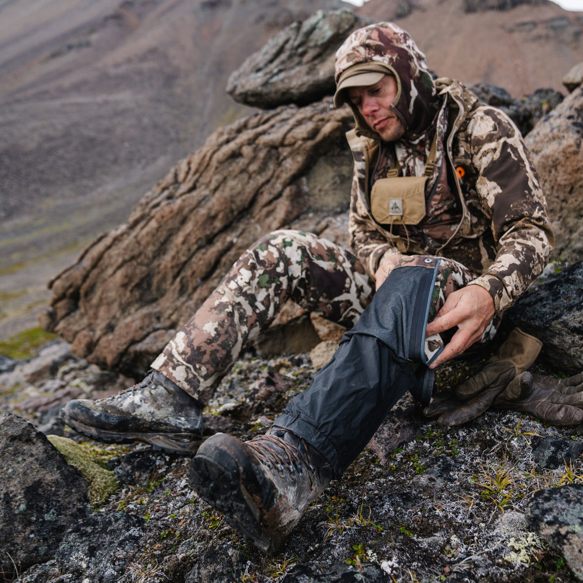 Black zippered gaiter being adjusted over a muddy hiking boot.