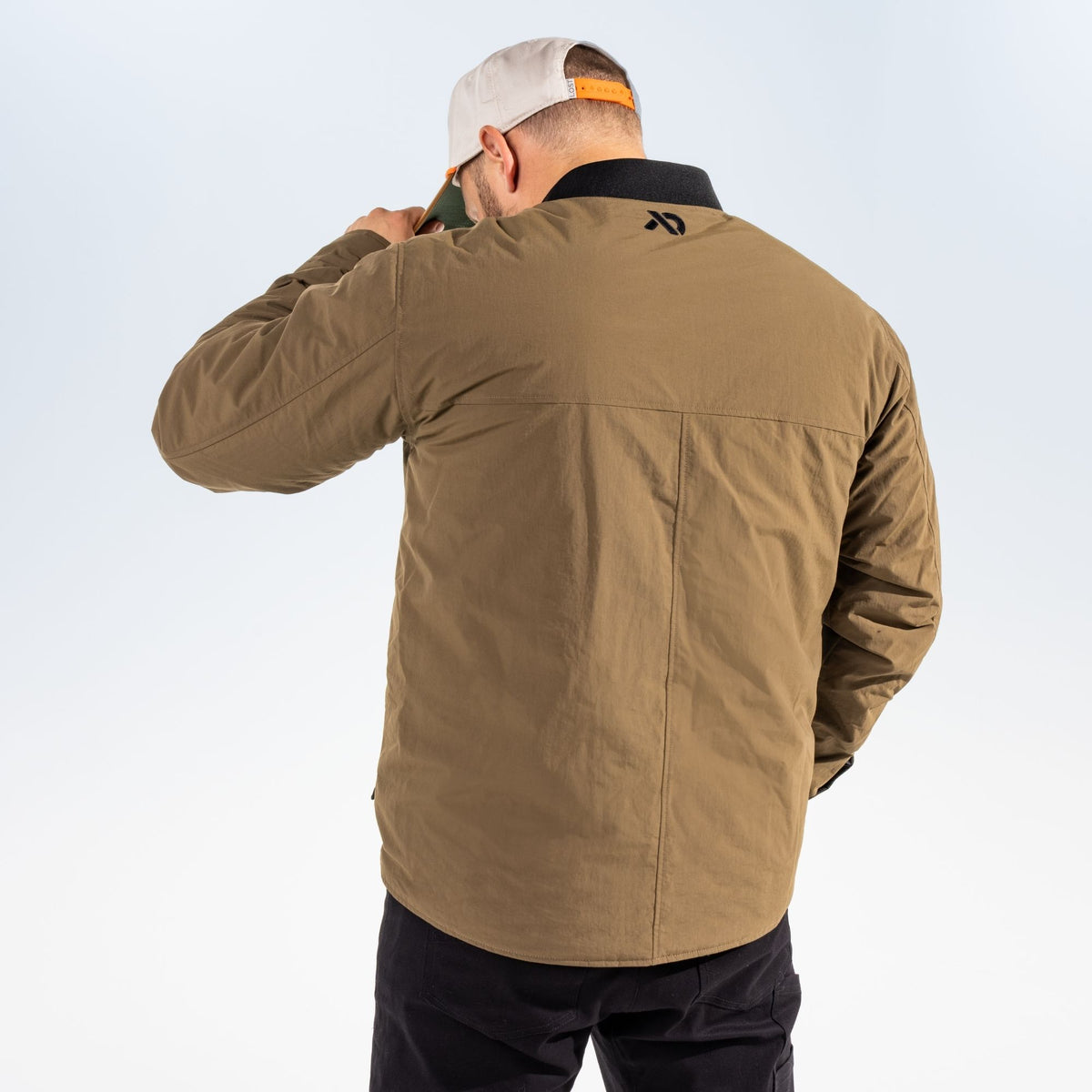 Reverse shot of a man wearing an akern chore coat with a FIRST LITE logo in the upper side of the back and a white hat against a light gray studio background