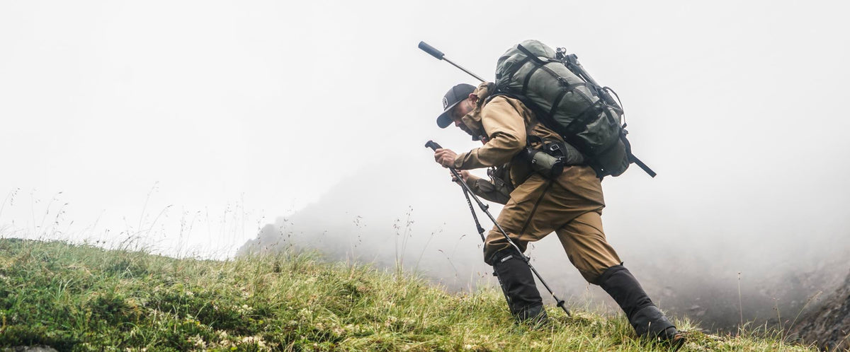 Olive green hunting backpack with rifle, worn by a man climbing a misty hill.