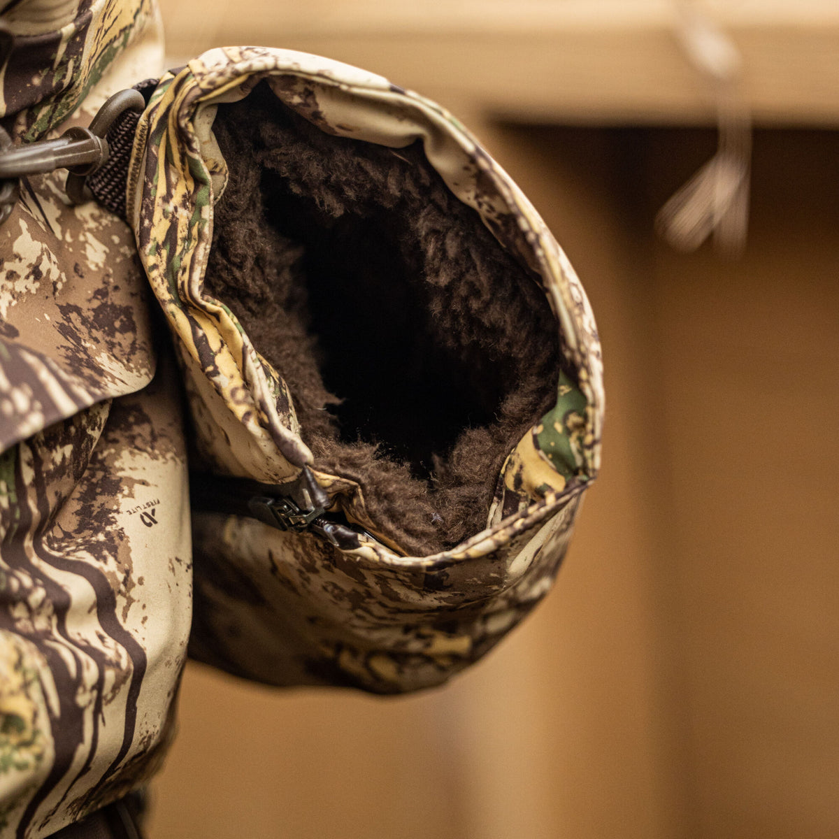 Camouflage hand warmer with a fuzzy dark brown interior, a visible zipper, and a clip attachment.