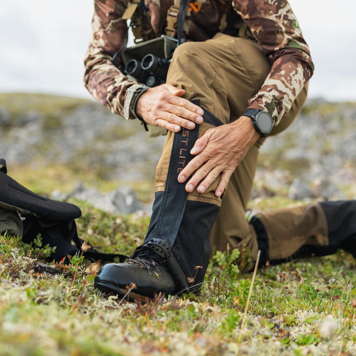 Man in the field adjusting boot gaiters in damp grass