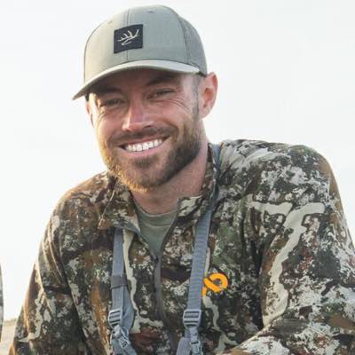 Olive green flat-brim cap with antlers logo, camo jacket with orange logo.