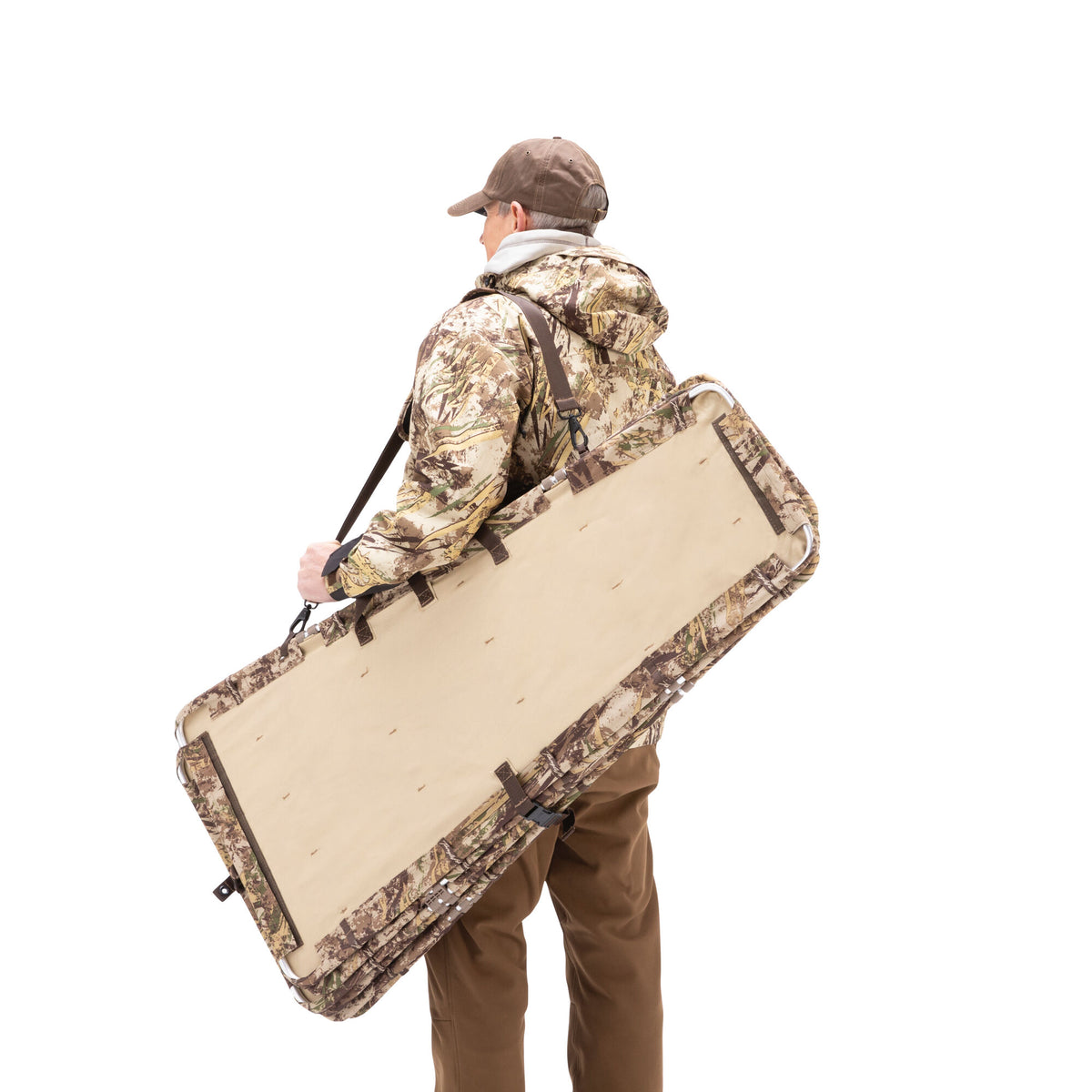 Folded tan and camouflage portable ground blind with shoulder strap, carried over a person's shoulder.