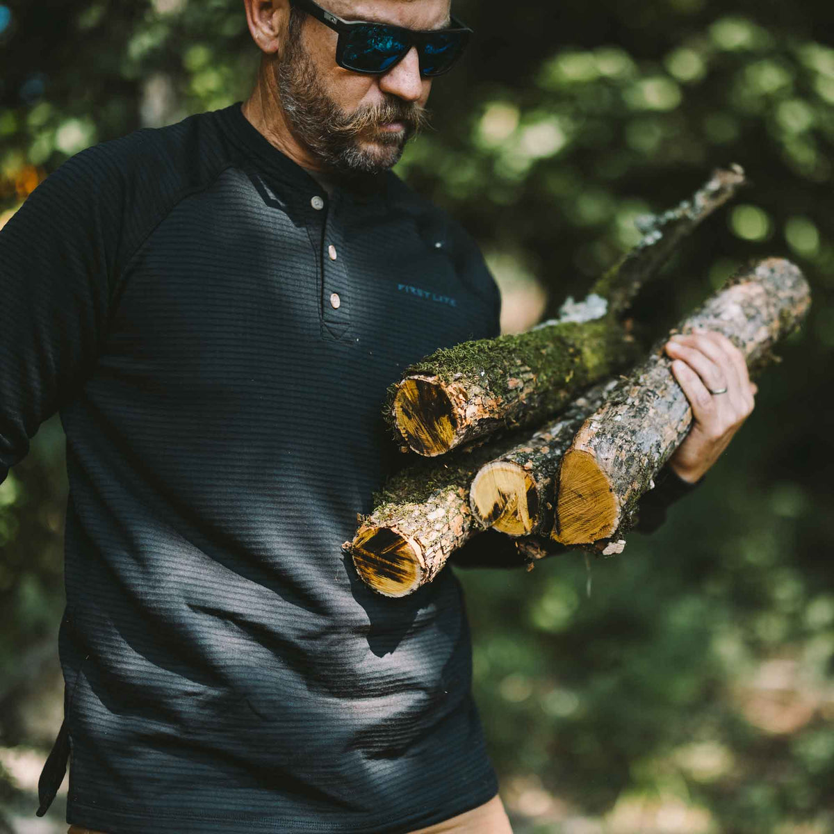 Black long-sleeve henley shirt featuring a subtle textured pattern, raglan sleeves, and a "FIRST LITE" logo.