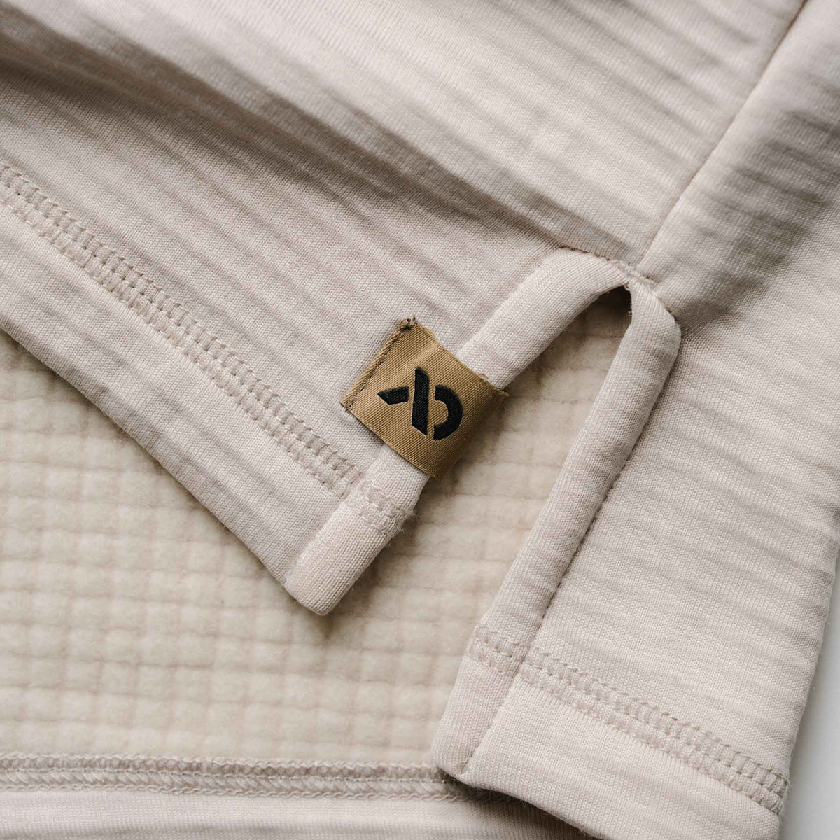 Oatmeal thermal shirt folded to reveal its ribbed exterior, waffle knit interior, and a brown brand tag with a black logo.