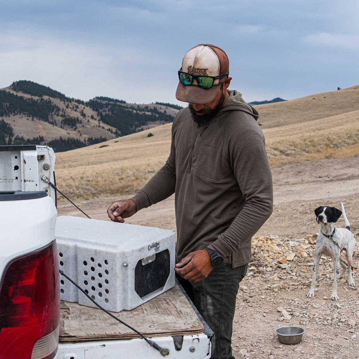 Man handles a speckled light gray CackleBox dog training crate with circular ventilation holes on a truck bed.
