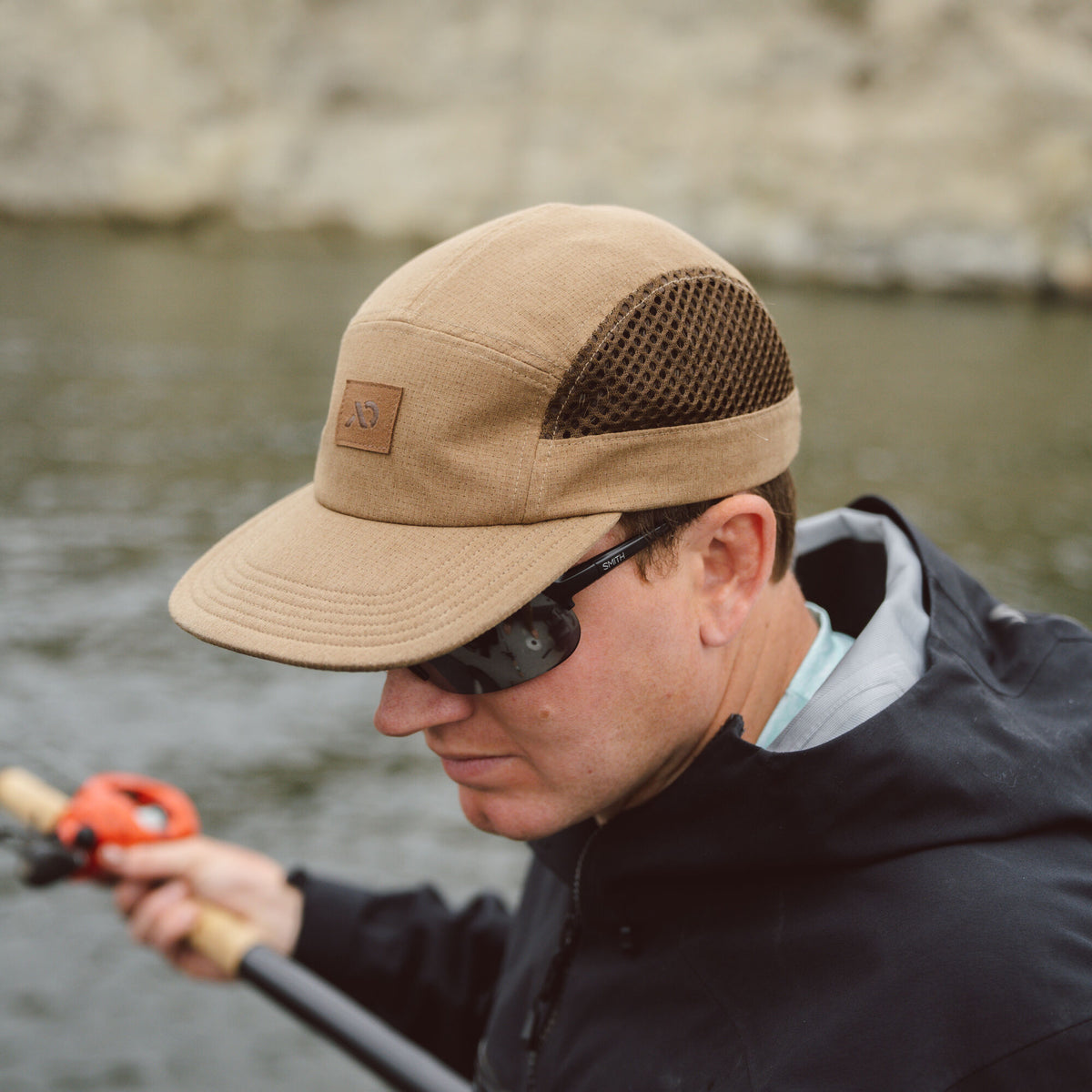 Tan 5-panel cap with a brown leather logo patch, dark brown mesh side panels, and a stitched brim.