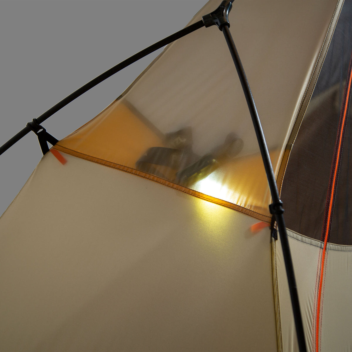 A beige tent with black poles and orange trim glows from an interior light, revealing blurry items inside.