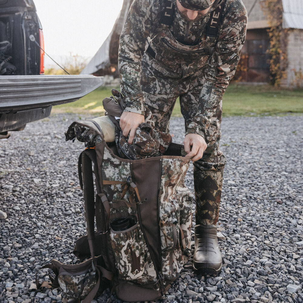 Brown and green camouflage hunting backpack with visible side pockets, being packed.