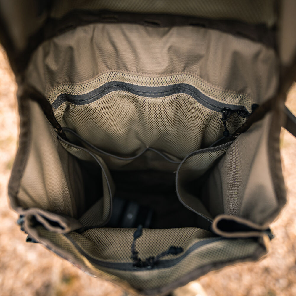 Olive green backpack interior with two mesh zippered top pockets, multiple open compartments, and a dark camera lens at the bottom.