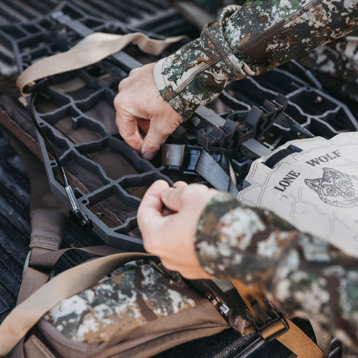 Close-up of a person handling a dark grey open-lattice hunting climbing stick with tan straps and a visible Lone Wolf brand tag.