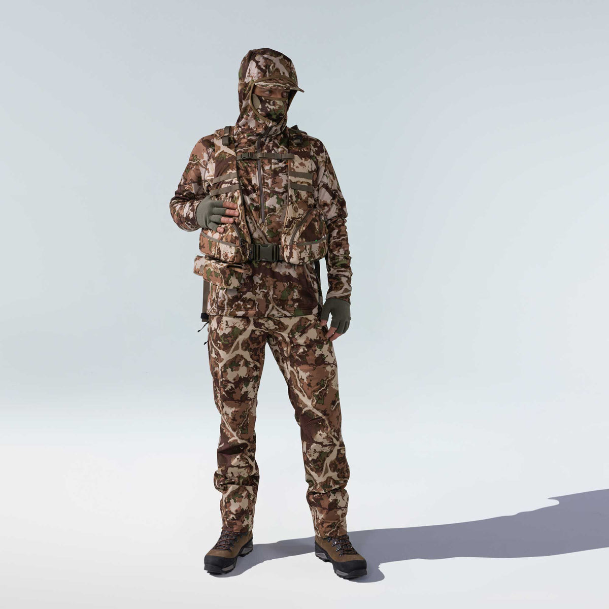 Full camouflage hunting suit in brown, green, and beige, featuring a hooded jacket, face mask, fingerless gloves, integrated chest rig, and matching pants with hiking boots.