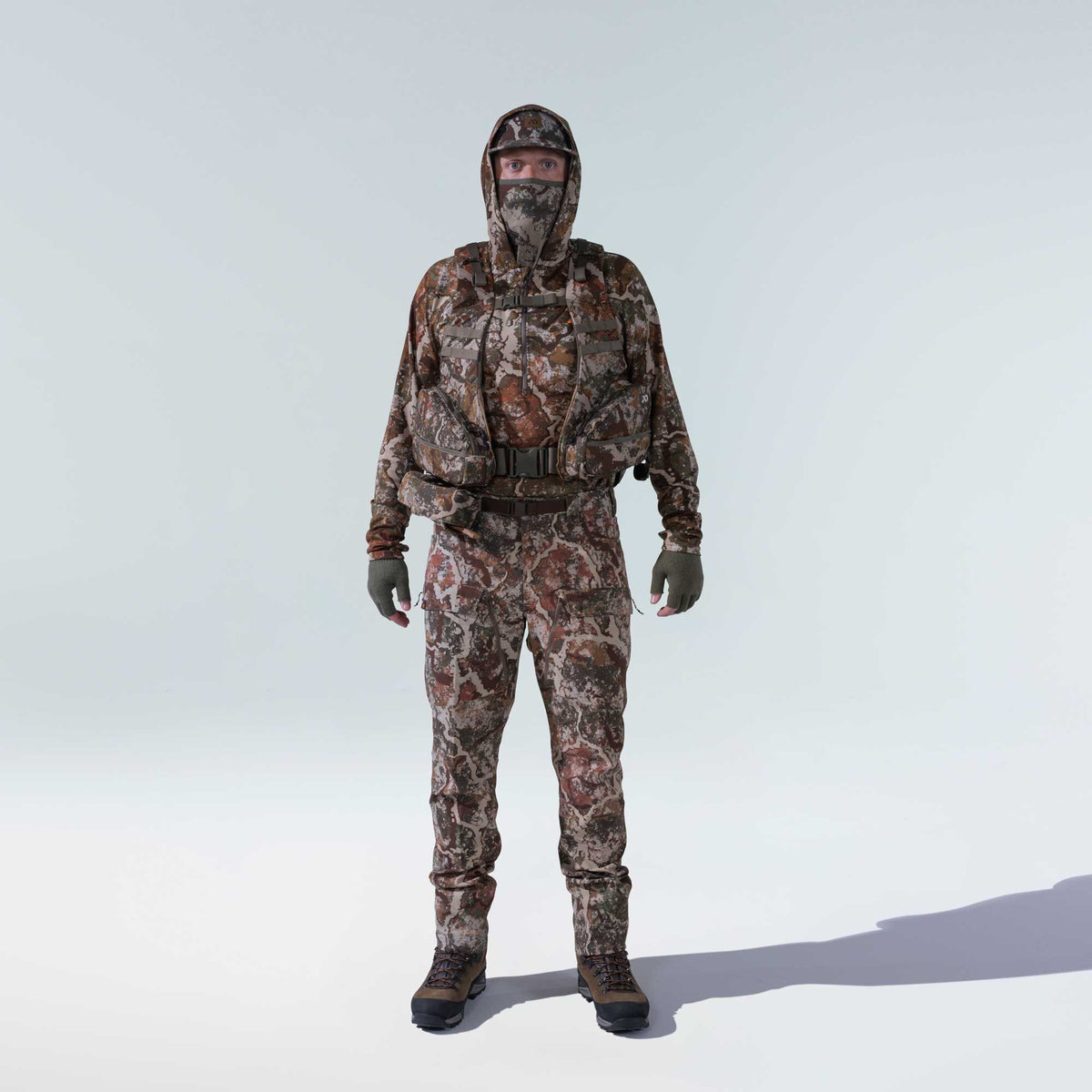 Full earth-toned camouflage hunting suit with hooded top, built-in face mask, chest rig, fingerless gloves, and brown boots.