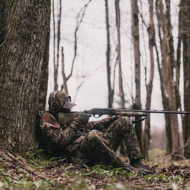 Semi-automatic shotgun with black barrel and olive drab stock, held by hunter.