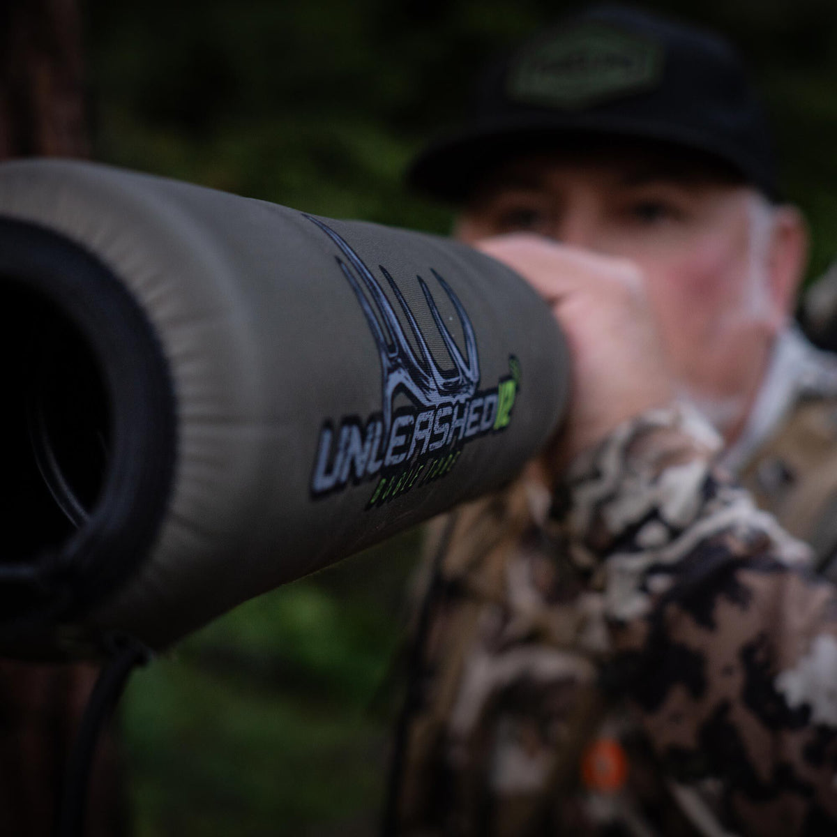 Olive green spotting scope cover with the "UNLEASHED" antler logo, held by a person in camouflage.