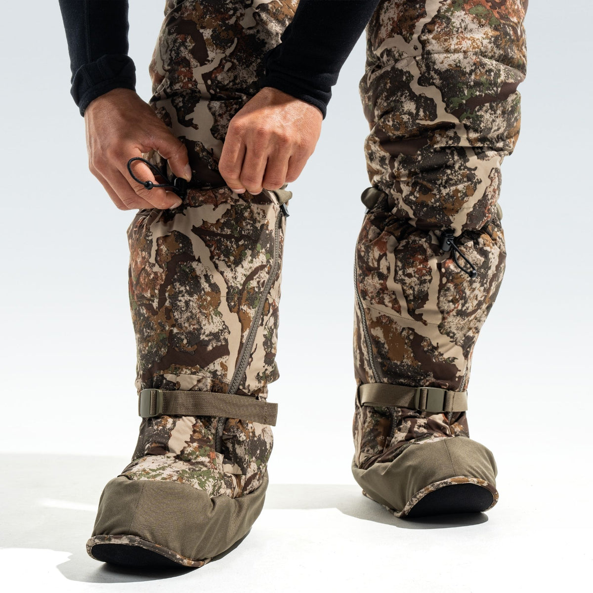 Man adjusting the fit of his camo overboots. 