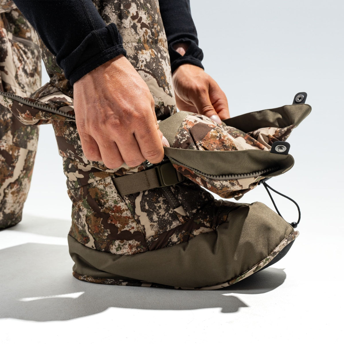 Man showing the interior of his camo overboot, he is wearing a camo pant and black shirt.