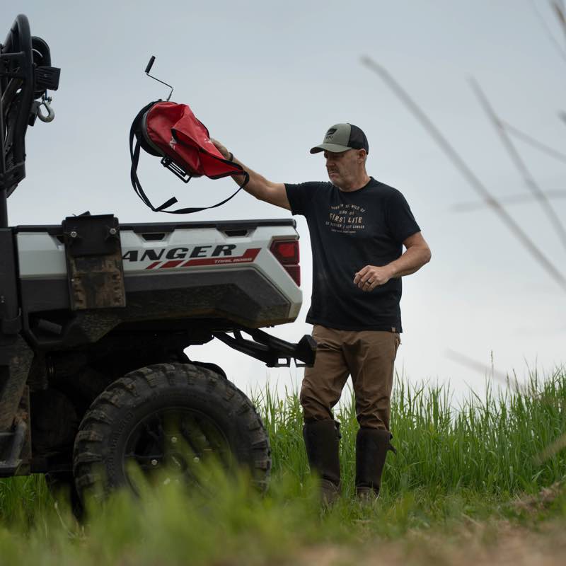 Red wildlife feeder with crank handle, held by a man near a Ranger UTV.