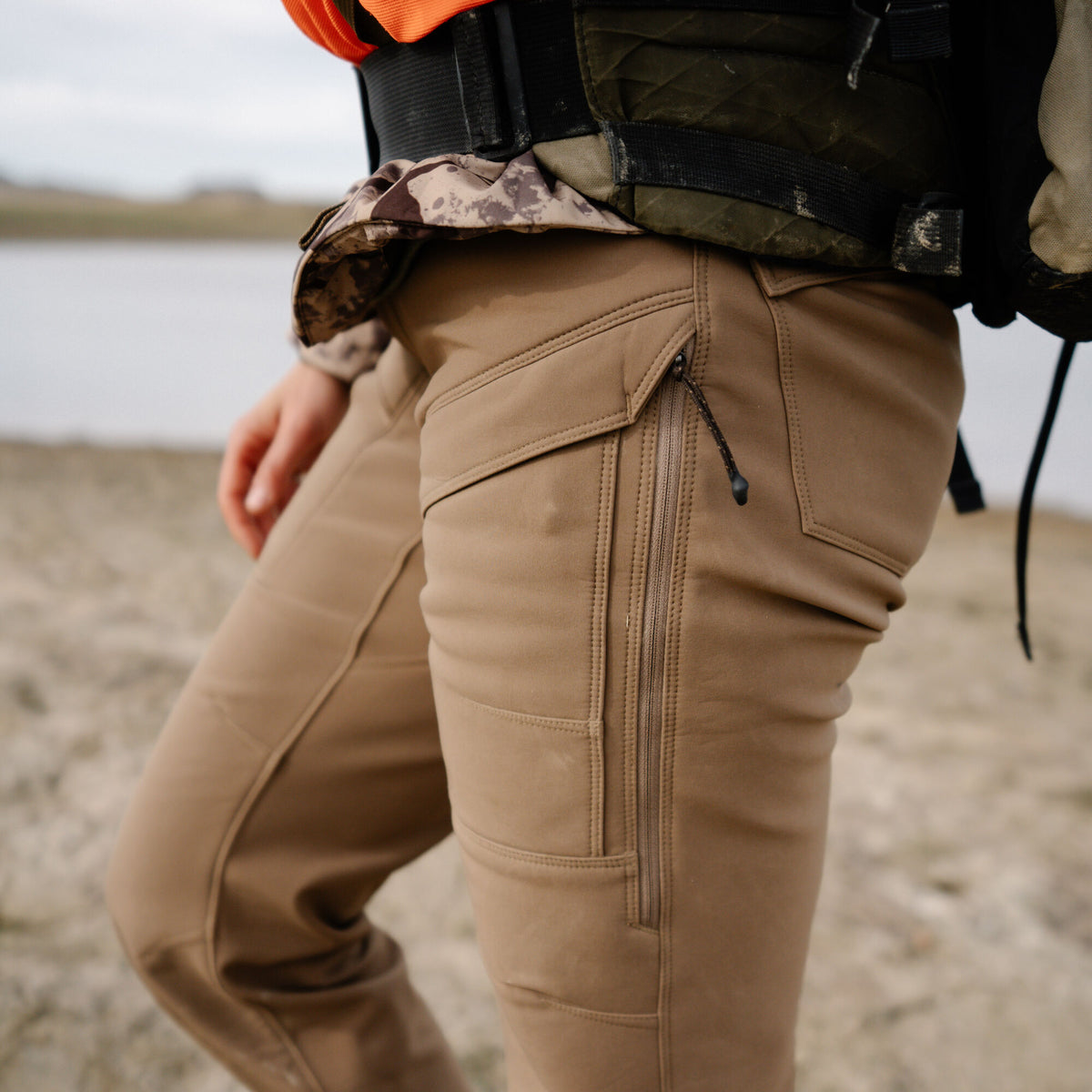 Tan outdoor pants with a zippered thigh pocket and an upper flap pocket.