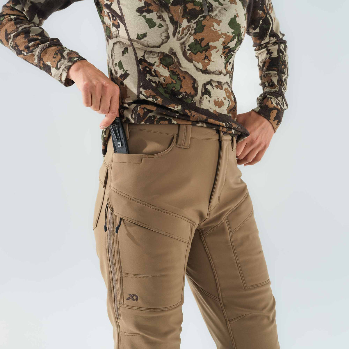 Tan outdoor pants with a knife in the front pocket, zippered thigh pockets, and articulated knee stitching.