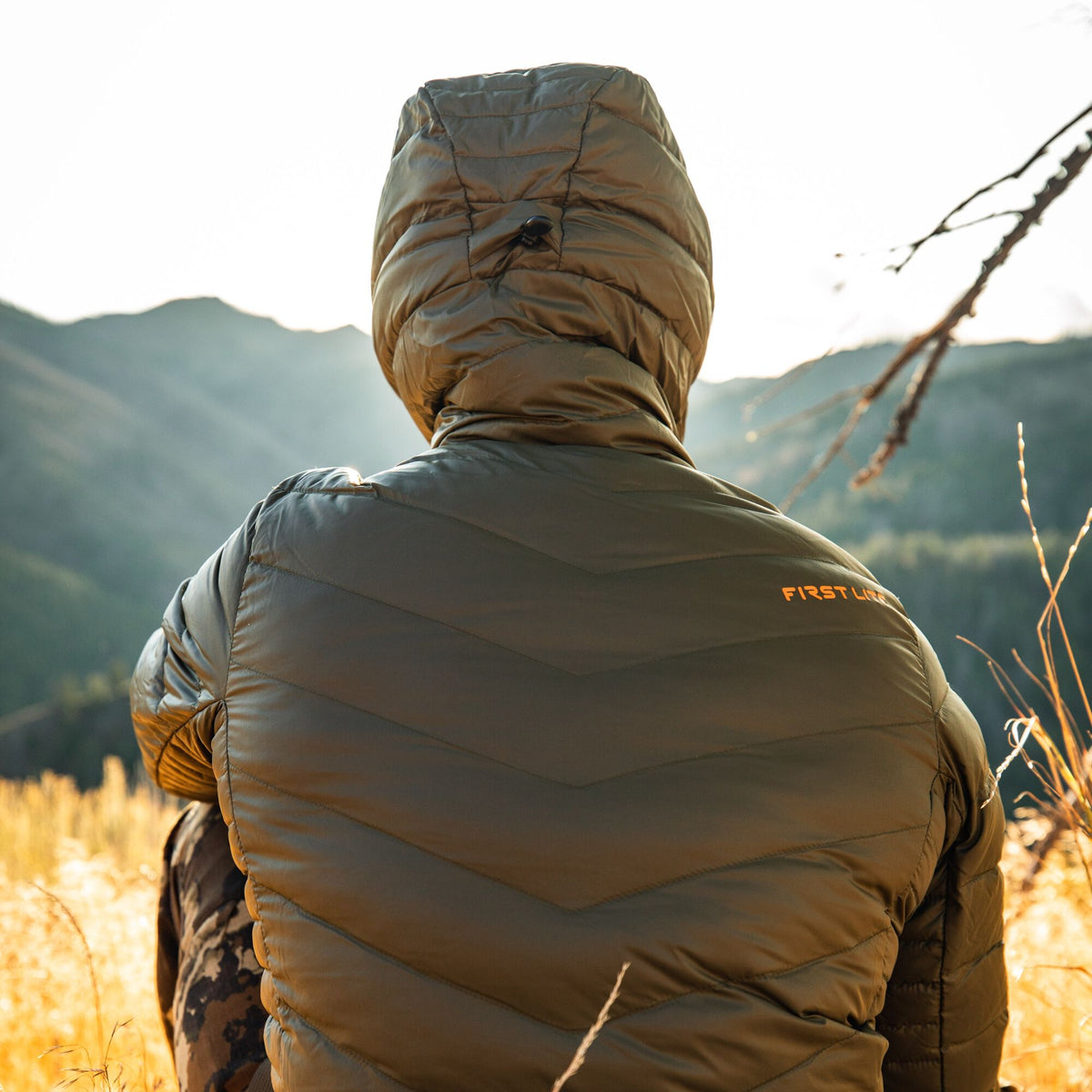 Olive green hooded puffer jacket featuring chevron quilting on the back and a "FIRST LITE" logo on the right shoulder.