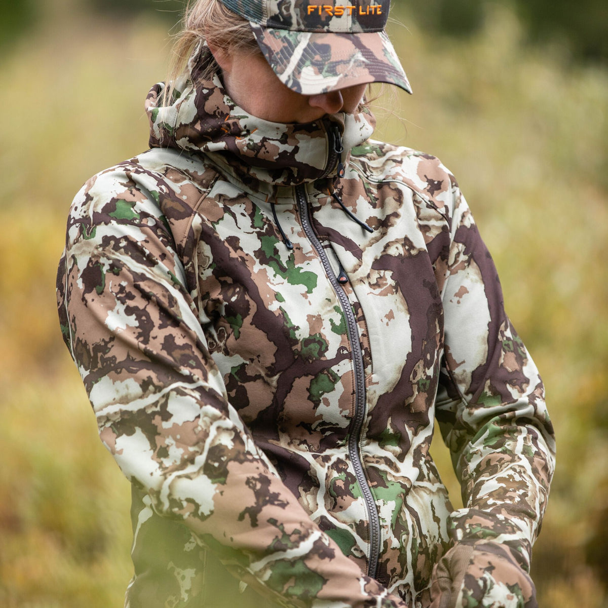 A person wears a First Lite Fusion camouflage full-zip hooded jacket and matching hat.