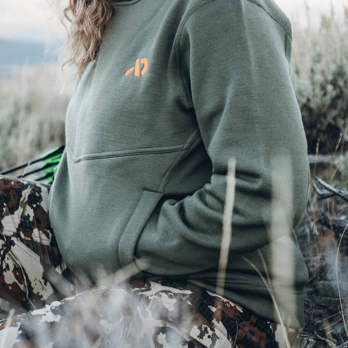 Olive green sweatshirt featuring an orange chest logo, a horizontal chest seam, and side pockets.