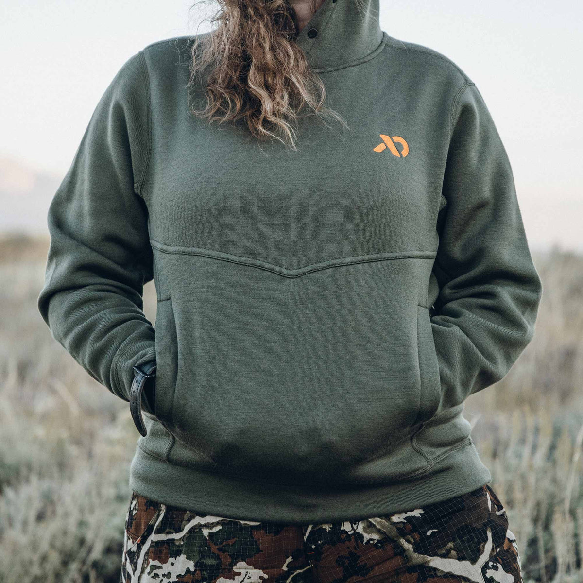 Olive green pullover sweatshirt with a buttoned collar, orange chest logo, V-shaped chest seam, and front kangaroo pocket.