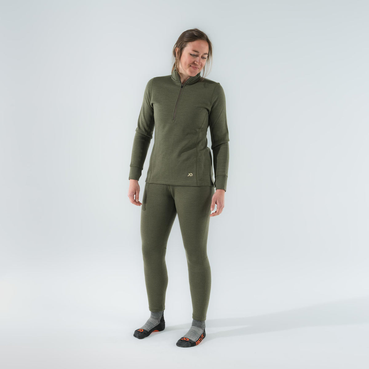 A woman models an olive green thermal base layer set with a quarter-zip long-sleeve top and matching leggings.