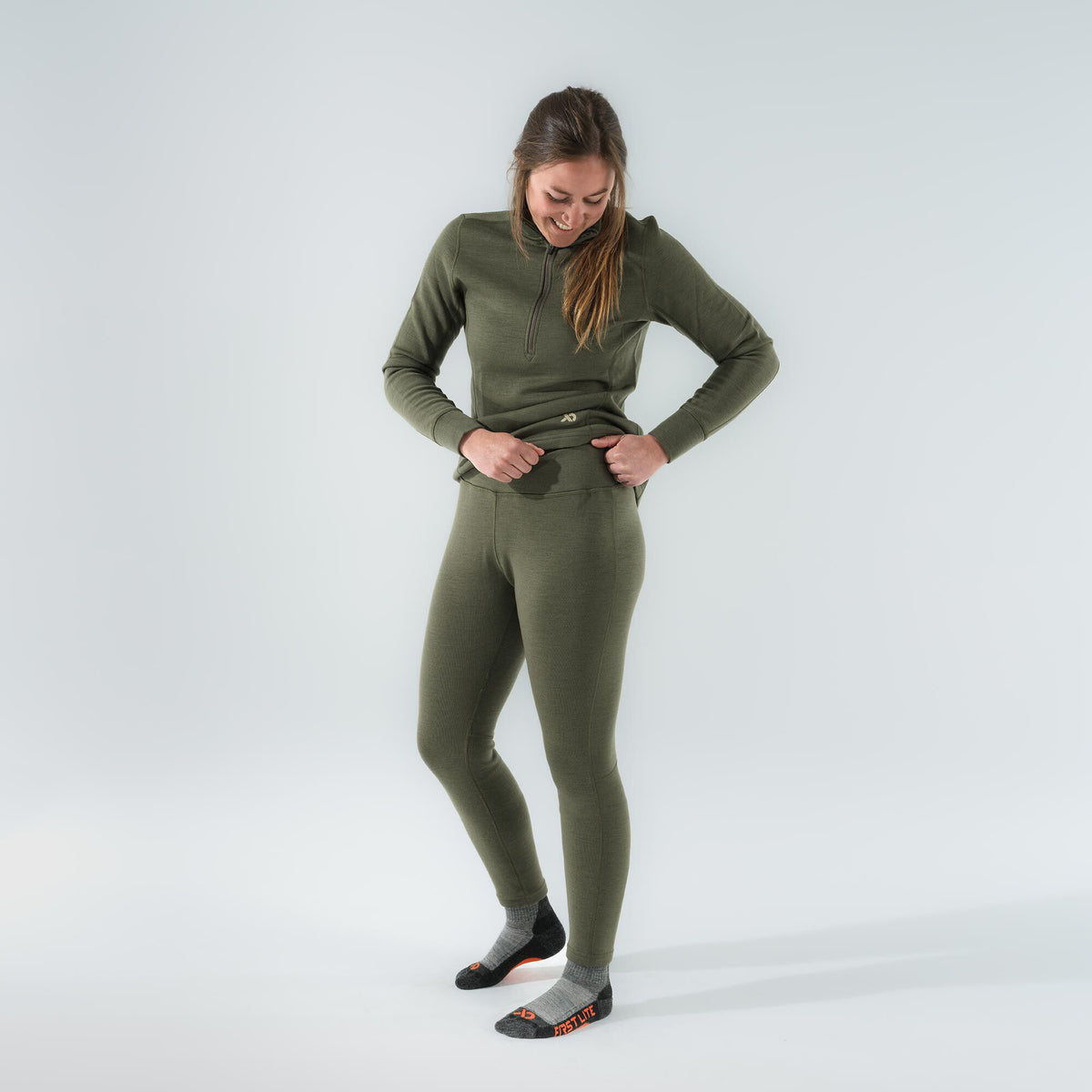 A woman wears an olive green thermal base layer set, including a quarter-zip long-sleeve top and leggings.
