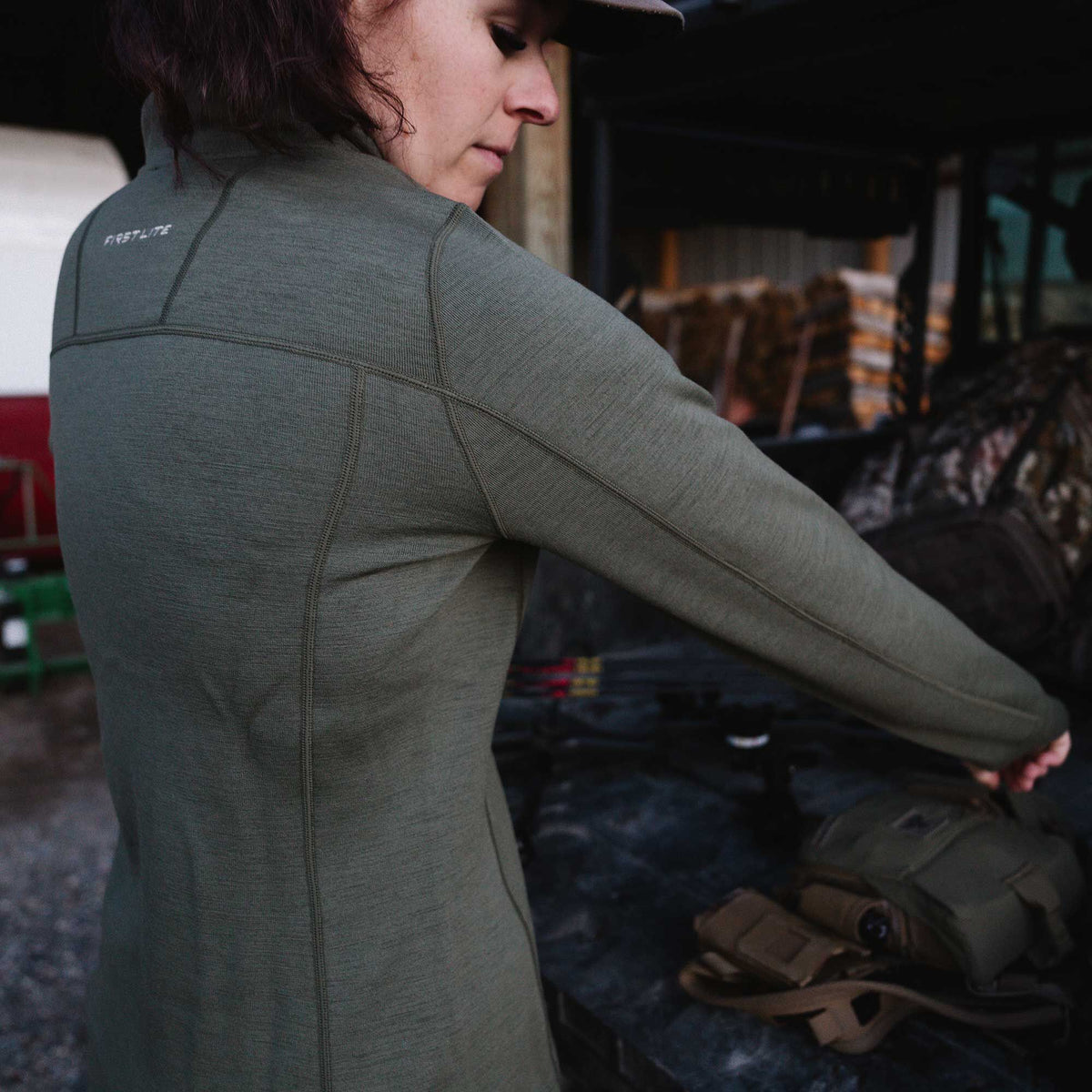 Dark green First Lite performance long-sleeve top with visible logo and detailed stitching on the back and shoulders.