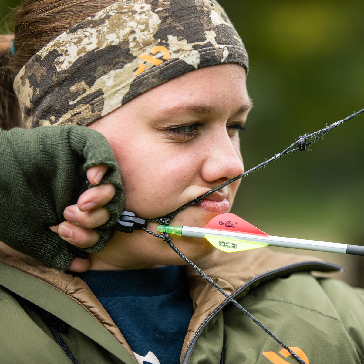 Wide camouflage fabric headband with an orange First Lite logo, worn by an archer.