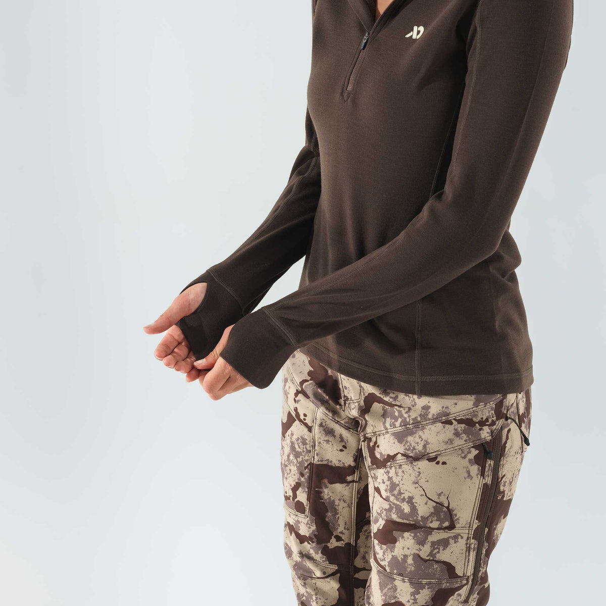 Brown quarter-zip long-sleeve top featuring thumbholes and a white chest logo.