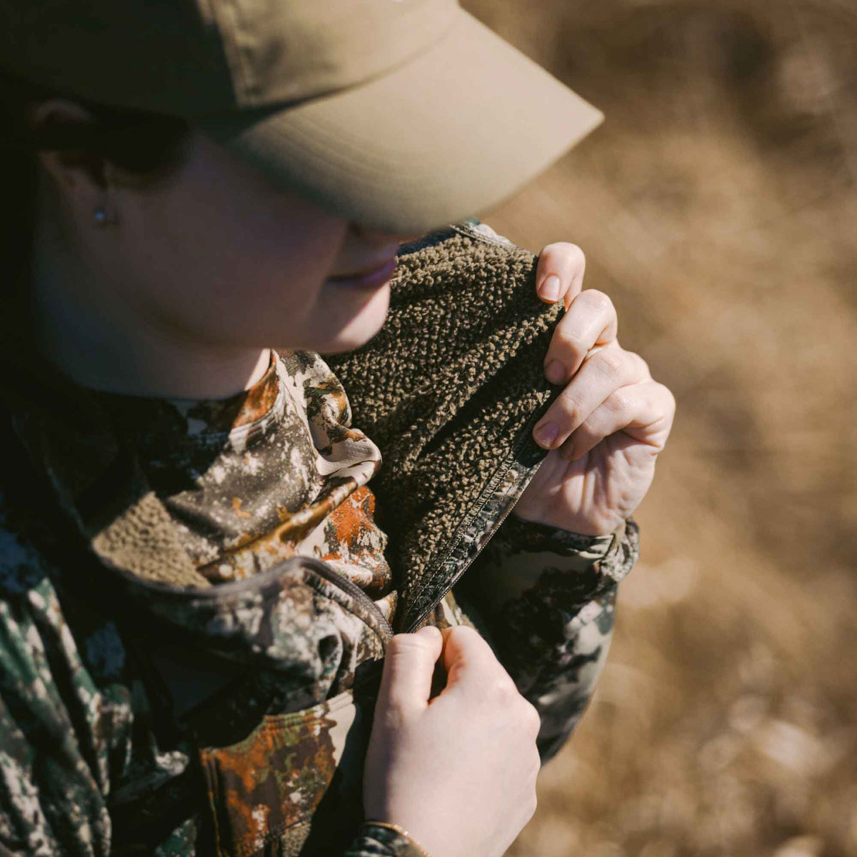 Close-up of a person wearing a camouflage jacket with a dark green fuzzy interior lining, adjusting the zipper.