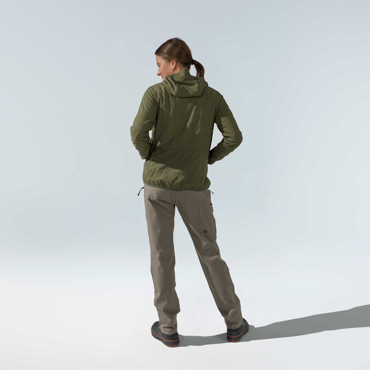 Back view of a woman wearing an olive green hooded jacket with subtle quilting and Walnut cargo pants.