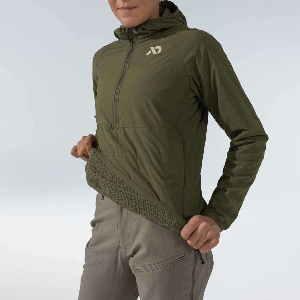 A person wears an olive green hooded jacket with a half-zip, padded torso, and textured fleece inner lining revealed at the hem.