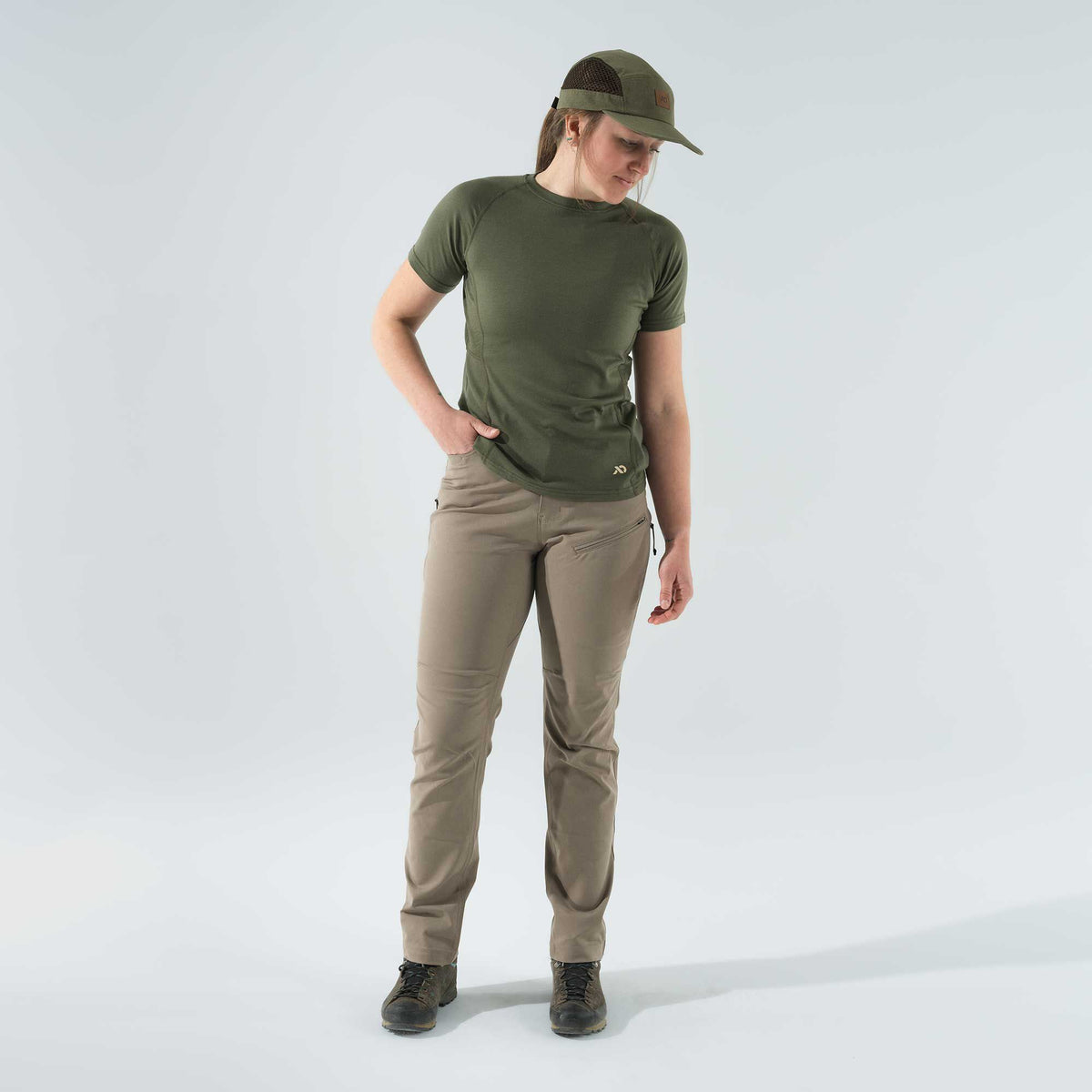 Woman wearing an olive green short-sleeve shirt, tan active pants with zippered pockets, and an olive green cap with mesh sides.