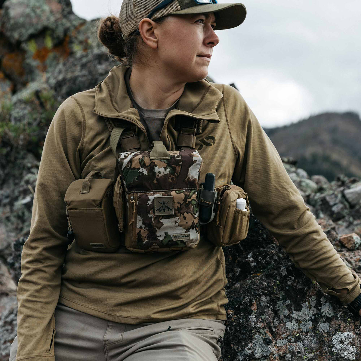 FHF Gear camouflage binocular chest harness worn by a woman, featuring tan accessory pouches holding a radio and a bottle.