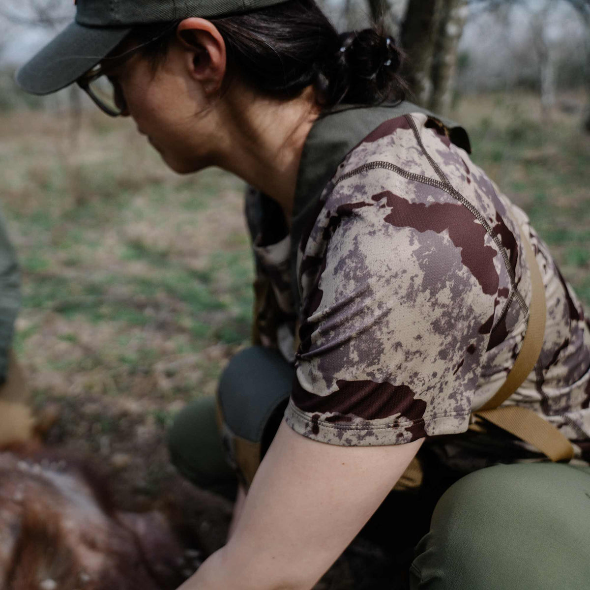 Short-sleeved camouflage top with brown, tan, and grey blotch pattern and visible flatlock stitching on the shoulders.